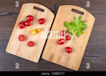 Geschnittene und ganze Tomaten auf zwei Schneidebrettern auf hölzernem Hintergrund. Draufsicht, flach. Stockfoto