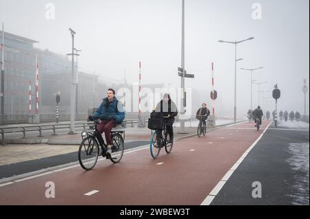 Pendler fahren an einem kalten, nebeligen Morgen am Bahnhof Amsterdam Centraal auf Radwegen zur Arbeit Stockfoto