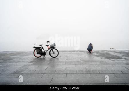 Frau, die einen Vogel an einem kalten Tag mit ihrem Fahrrad auf einem Stand in der Nähe fotografiert Stockfoto