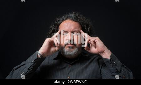 Porträt eines lateinischen Mannes mit weißem Bart und schwarzem Lockenhaar mit konzentriertem Ausdruck, mit den Fingern auf den Schläfen in der Hand, mit schwarzem s Stockfoto