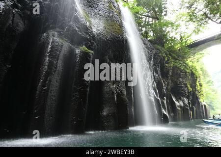 Eine malerische Landschaft mit einem majestätischen Wasserfall, der eine felsige Klippe hinunterstürzt, mit kleinen Booten, die friedlich auf dem kristallklaren Wasser schwimmen Stockfoto