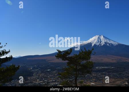 Eine malerische Winterlandschaft mit einem majestätischen, schneebedeckten Berg, umgeben von zahlreichen Kiefern und kleinen Gebäuden im Vordergrund Stockfoto