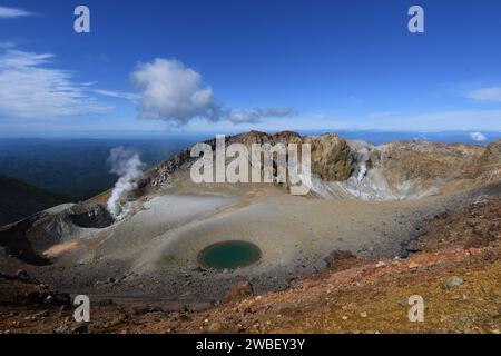 Eine atemberaubende natürliche Landschaft mit einer heißen Quelle, eingebettet in einen Berghang, umgeben von üppigem Laub und einem lebendigen blauen Himmel Stockfoto