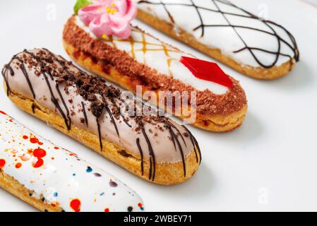 Wunderschöne, köstliche französische Eclairs mit originalem cremefarbenem Dekor auf weißem Teller. Leckere bunte Dessert-Profiteroles Stockfoto