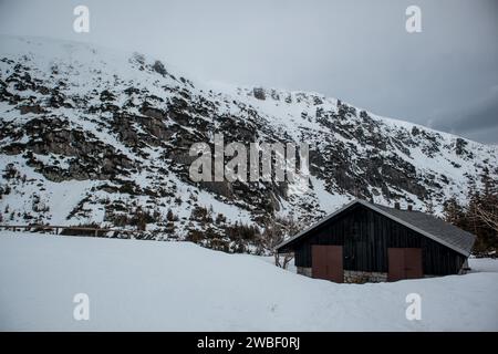 Eine einsame Hütte befindet sich unter einer zerklüfteten, schneebedeckten Berglandschaft unter einem bewölkten Himmel. Polen, Karpacz, Karkonosze Stockfoto