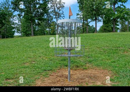 Ein Disc-Golfkorb mit einer Farbfahne oben auf einem Hügel im Wald bei Blick auf den Park in der Nähe an einem sonnigen Tag im Spätsommer Stockfoto