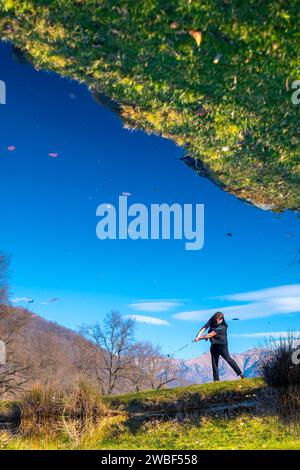 Männlicher Golfer reflektierte sich in einem Wasserteich und schlug den Golfball auf dem Fairway auf dem Golfplatz mit Mountain an einem sonnigen Tag in der Schweiz Stockfoto