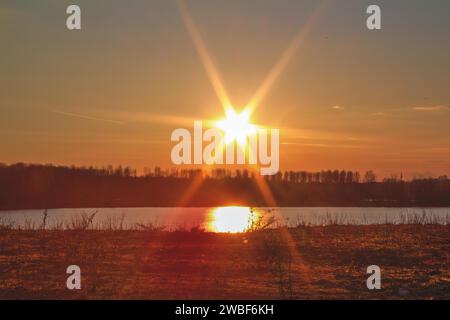 Die Sonne untergeht über einem ruhigen See und taucht die Landschaft in warmes, goldfarbenes Licht, Elbsee, Hilden, Nordrhein-Westfalen, Deutschland Stockfoto