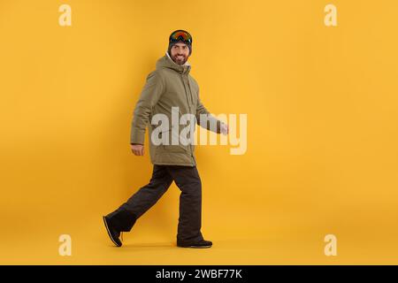 Wintersport. Glücklicher Mann in Skianzug und Brille, der auf orangefarbenem Hintergrund läuft Stockfoto