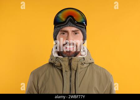 Wintersport. Glücklicher Mann in Skianzug und Brille auf orangem Hintergrund Stockfoto