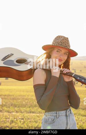 Schöne, glückliche Hippie-Frau mit Gitarre im Feld Stockfoto