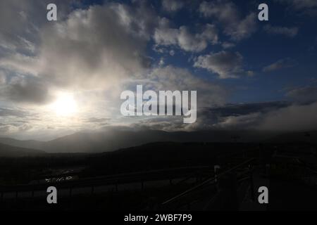 Eine Holzbank steht auf einer natürlichen, grasbewachsenen Lichtung, umgeben von Bäumen und Wolken am Himmel Stockfoto