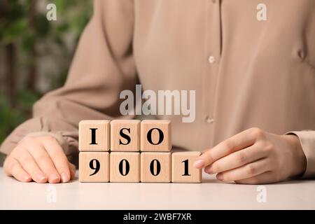 Frau, die die Abkürzung ISO und Nummer 9001 von Holzwürfeln auf weißem Tisch macht, Großaufnahme Stockfoto