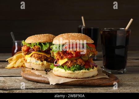 Köstliche Burger mit knusprigem Chicken Patty, Pommes Frites und Limonaden auf Holztisch Stockfoto