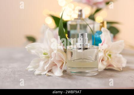 Flaschen Parfüm und schöne Lilienblüten auf dem Tisch vor beigem Hintergrund mit verschwommenem Licht, Nahaufnahme Stockfoto