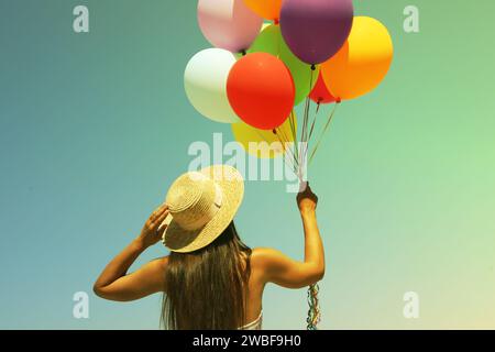 Frau, die einen Haufen bunter Ballons am sonnigen Tag gegen den Himmel hält, Rückansicht Stockfoto