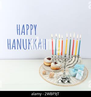 Happy Hanukkah. Menora, Donuts, Dreidels und Geschenke auf weißem Tisch Stockfoto