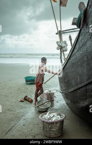 Fischer mit seinem Boot am Strand mit dem Fang des Tages während eines Monsunschauer, Cox's Bazar, Bangladesch Stockfoto