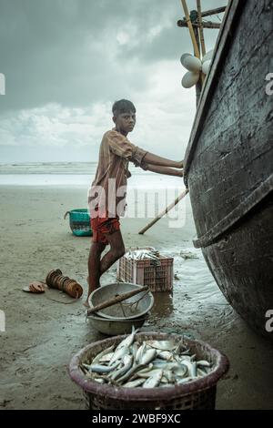 Fischer mit seinem Boot am Strand mit dem Fang des Tages während eines Monsunschauer, Cox's Bazar, Bangladesch Stockfoto