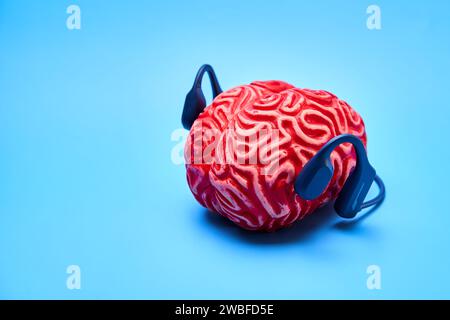 Rotes Gummigehirn mit Kopfhörern auf blauer Oberfläche. Brain Rest-Konzept. Stockfoto