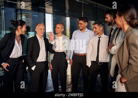 Attraktiver grauhaariger Kaukasischer Teamleiter glückliche Begrüßung der Mitarbeiter verschiedener formeller Profis. Stockfoto