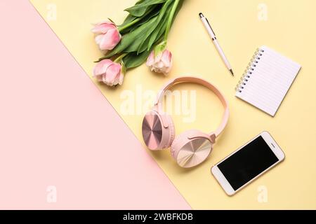 Moderne Kopfhörer, Mobiltelefon, Notebook und Tulpenblumen auf farbigem Hintergrund Stockfoto