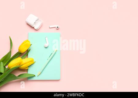 Moderne Kopfhörer, Notizbuch, Stift und wunderschöne Tulpenblumen auf pinkfarbenem Hintergrund Stockfoto