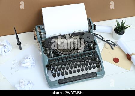 Vintage-Schreibmaschine, Brille, Stifthalter, Umschlag und Schriftrollen mit Siegelstempel aus Wachs auf weißem Tisch in der Nähe der braunen Wand Stockfoto