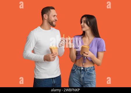 Wunderschönes junges Paar mit Pommes frites auf orangefarbenem Hintergrund Stockfoto