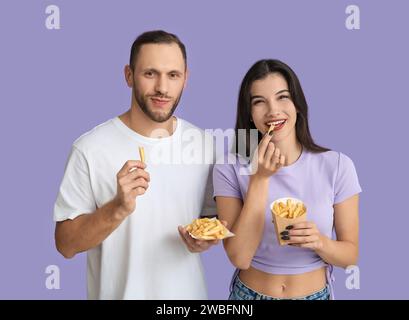 Schönes junges Paar, das Pommes frites auf lila Hintergrund isst Stockfoto