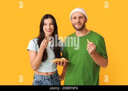 Schönes junges Paar mit Pommes frites auf gelbem Hintergrund Stockfoto