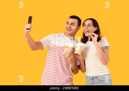 Ein junges Paar, das Pommes frites hält und Selfie auf gelbem Hintergrund macht Stockfoto