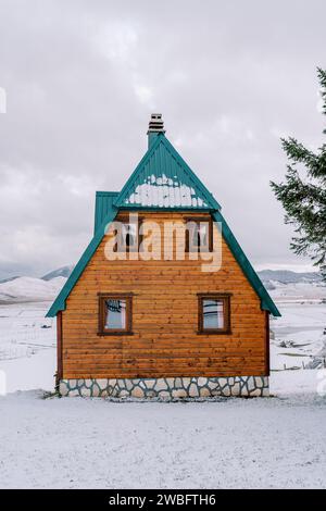Holzhaus mit grünem Dach in einem schneebedeckten Bergtal Stockfoto