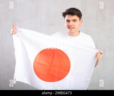 Ein Mann mittleren Alters hält die unaufgerollte Flagge Japans in den Händen, die über dem Kopf gegen eine graue Wand gerichtet sind Stockfoto
