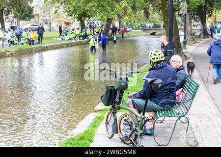 Männlicher Radfahrer in Bourton auf dem Wasser mit einer Brompton x Bear Grylls C Line Erkunden Sie das Faltrad, unterhalten Sie sich mit einem Freund aus England, Großbritannien, 2023 Stockfoto