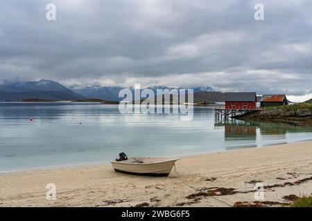 Weißes Ruderboot am weißen Sandstrand von Sommarøy in Troms, Norwegen. Yacht im Hintergrund das türkisfarbene Wasser des Atlantiks mit Inseln Stockfoto