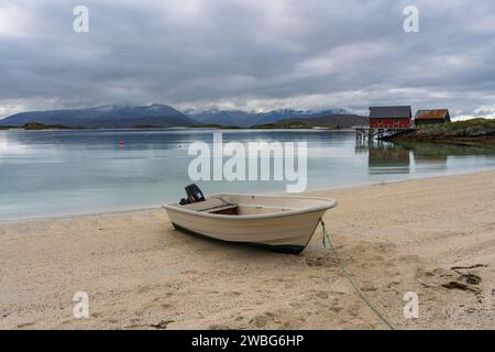 Weißes Ruderboot am weißen Sandstrand von Sommarøy in Troms, Norwegen. Yacht im Hintergrund das türkisfarbene Wasser des Atlantiks mit Inseln Stockfoto