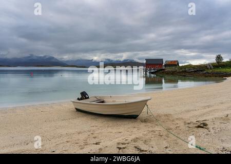 Weißes Ruderboot am weißen Sandstrand von Sommarøy in Troms, Norwegen. Yacht im Hintergrund das türkisfarbene Wasser des Atlantiks mit Inseln Stockfoto