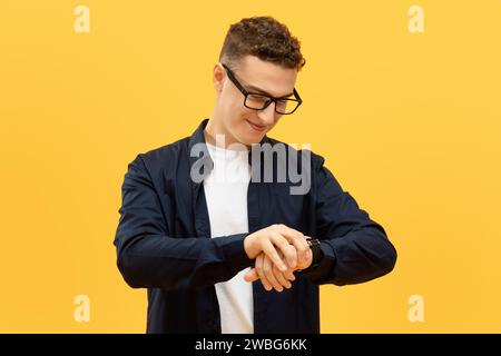 Positiver junger Kerl mit Brille, der die Zeit überprüft Stockfoto