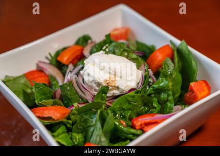 Eine weiße Keramikschale gefüllt mit einem bunten, frischen Salat steht auf einem Holztisch in einem Essbereich Stockfoto