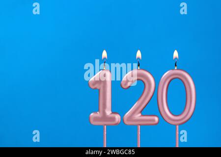 Nummer 120 - brennende Geburtstagskerze auf blauem schaumigem Hintergrund Stockfoto