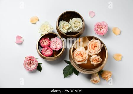 Tibetische Klangschalen mit Wasser und verschiedenen schönen Rosenblüten auf weißem Hintergrund, flach gelegen Stockfoto