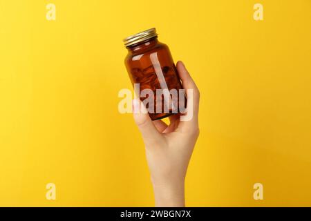 Frau, die ein Glas mit Vitaminkapseln auf gelbem Hintergrund hält, Nahaufnahme Stockfoto