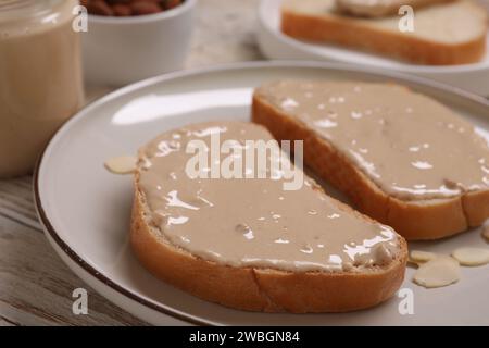 Toast mit leckerer Nussbutter und Mandelflocken auf Holztisch, Nahaufnahme Stockfoto