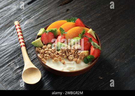 Joghurtschale mit frischen Beeren, Müsli, Avocado und Pfirsich auf Holztisch Stockfoto