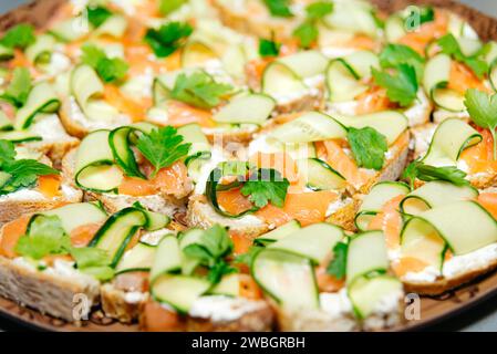 Räucherlachs-Canapes mit Frischkäse, Gurke und frischer Petersilie, auf einem Tablett für eine raffinierte Vorspeise. Stockfoto