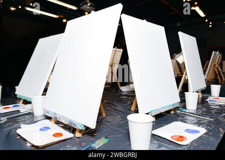 Leere Leinwände auf Staffeleien mit Acrylfarben für einen Kunstworkshop oder Malkurs in einem kreativen Studio. Stockfoto