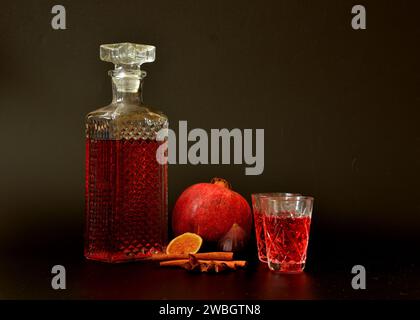 Granatapfel-Feigen-Likör mit Zimt und Anis auf schwarzem Hintergrund, hausgemachter Alkohol in einer Karaffe und zwei Gläser neben Reifen Früchten. Nahaufnahme. Stockfoto