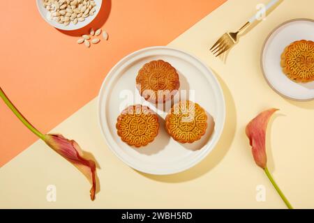Hintergrund mit Korallen- und Beigetönen waren zwei Gerichte mit Mondkuchen und ein Gericht mit Kürbiskernen. Das Herbstfest wird nach und nach zu einem Familienurlaub Stockfoto