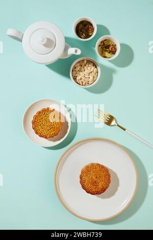 Flacher Blick auf zwei Mondkuchen auf weißen Tellern, die mit einem Tee-Set und einer Keramikschale mit Kürbiskernen angeordnet sind. Chinesen haben viele aufregende und einzigartige Menschen Stockfoto